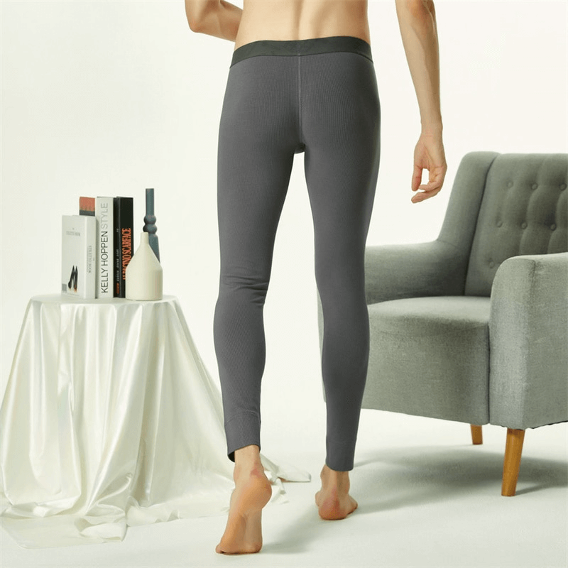 Man wearing tight-fitting gray elastic thermal pants, standing near a gray chair and white table.